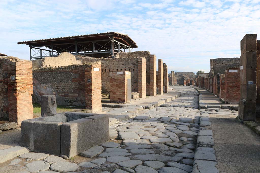 Fountain outside VII.14.13 and VII.14.14 on Via dellAbbondanza, Pompeii. December 2018. 
Looking east from fountain towards junction of Vicolo del Lupanare, on left, and Via dei Teatri, on right. 
Photo courtesy of Aude Durand.

