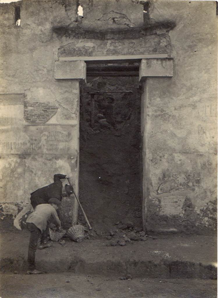 I.I.7.1 Pompeii. 6th January 1923. Entrance during excavation. Visible on each side of the doorway are the remains of electoral recommendations. Photo courtesy of Drew Baker. According to Varone and Stefani, immediately to the left of the door were a large number of electoral recommendations. To the right of the door were the electoral recommendations CIL IV 7196-8. See Varone, A. and Stefani, G., 2009. Titulorum Pictorum Pompeianorum, Rome: Lerma di Bretschneider. (p. 74

The remains of CIL IV 7212, CIL IV 7215, CIL IV 7210 (left) and CIL IV 7196 and 7197 (right) can be seen in this photograph. 

According to Epigraphik-Datenbank Clauss/Slaby (See www.manfredclauss.de) these read as:

Veientonem
aed(ilem) Primanus rog(at)       [CIL IV 7212]

L(ucium) Albucium
aed(ilem) o(ro) v(os) f(aciatis)      [CIL IV 7215]

L(ucium) Popidium Ampliatum
aed(ilem) Paquius rog(at)      [CIL IV 7210]

C(aium) Lollium Fuscum
aed(ilem) o(ro) v(os) f(aciatis)       [CIL IV 7196 ]

P(ublium) Paquium Proculum
[du]umvirum i(ure) d(icundo) vicini cupidi faciunt       [CIL IV 7197]

