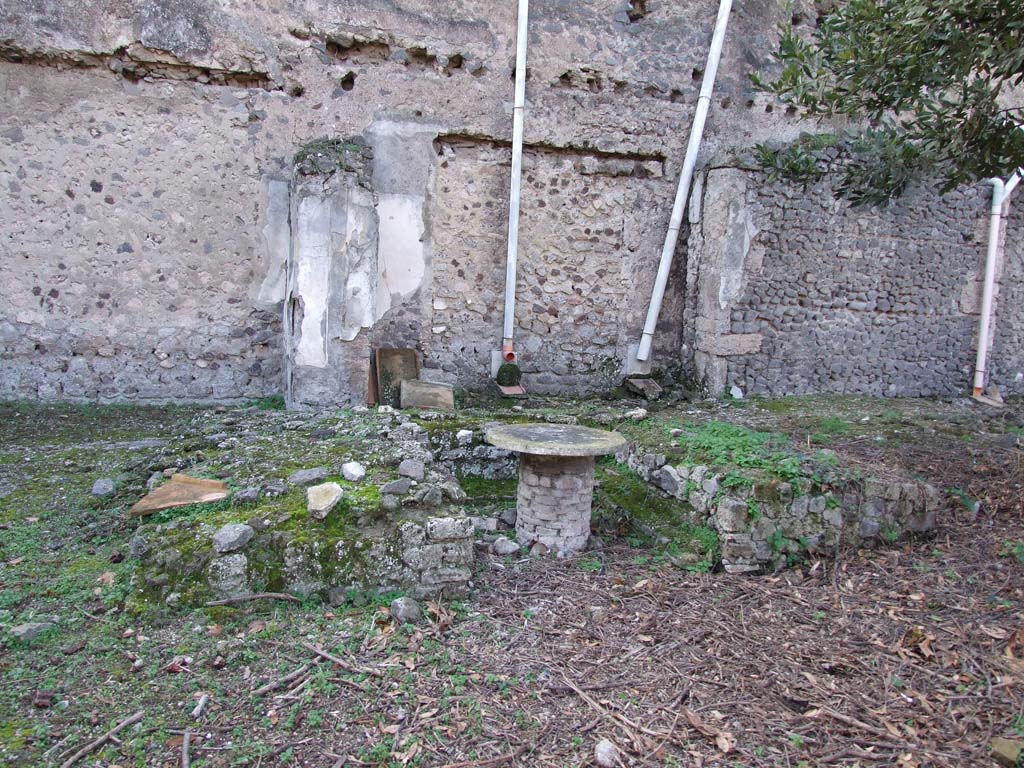 V.2.i Pompeii. December 2007. Room 25, triclinium with table in centre, which had a fountain pipe at its centre. 
According to Soprano -
Ubicazione: giardino. L. medius, m.4.45; l. summus e l. Imus, m.300; diametro della mensa, m. 0.80.
Bibliog: “Not.Scavi”, 1896, p.433; 1910, p.326 e ill.; “Rom. Mitt.”, 1895, p.147; Mau. Pompeji in Leben und Kunst (Lipsia, 1908), p.259;
Paoli, U.E., Vita romana, tav. xix.
Il triclinio, situato al centro del lato occidentale del giardino, a distanza del muro di fondo, presenta nei letti laterali una eguale lunghezza.
Attualmente i tre letti appaiono completamente grezzi. 
(Note 2: Al momento della scoperta i piani dei tre letti mostravano ancora avanzi di signino, le pareti esterne tracce d’intonaco rosso, e quelle interne tracce d’intonaco giallo: egualmente rivestita d’intonaco giallo appariva la mensa.)
La mensa, circolare, era rivestita da una lastra di marmo bianco, con al centro un foro per la fuoruscita di un getto d’acqua.
Lungo le pareti interne dei tre letti corre un gradino che sporge di cm.25.
Di fronte al triclinio, al centro del giardino, si apre il bacino d’una vasca rettangolare: nel mezzo di essa s’eleva una colonnina rivestita di signino come le pareti della vasca. A pie del l. summus c’era un canaletto per la raccolta delle acque.
See Soprano, P. (1950). I triclini all’aperto di Pompei. (In Pompeiana, raccolta di studi per il secondo centenario degli scavi di Pompei. Napoli, Gaetano Macchiaroli, Editore, P. 298, no.9). 
