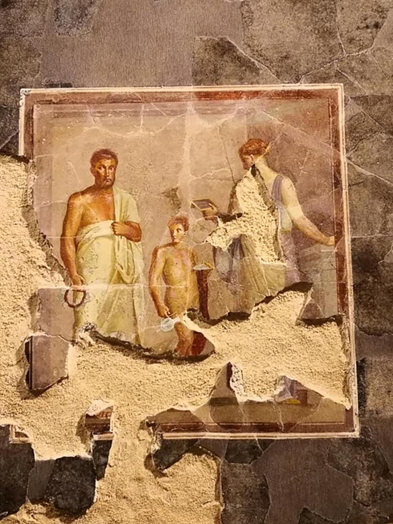 VI.17.42 Pompeii. December 2019. 
Fragments of a dining room fresco from the centre of a wall, thought to be the poet Euphorion.
On display in exhibition “Pompei e Santorini” in Rome, 2019. Photo courtesy of Giuseppe Ciaramella.
A female (poetess?) is reading a diptych, and a boy with a red cloak has a plate for offerings.
Parco Archeologico di Pompei, inventory number 86075. 
This is part of a larger panel, one of several items recomposed from a large number of fragments found in a channel in the garden. 
It is thought to be from the reconstruction work following the damage after the earthquake of AD62. 
Its original room location is unknown.
See Aoyagi M. and Pappalardo U., 2006. Pompei (Regiones VI-VII) Insula Occidentalis. Napoli: Valtrend. (p. 222-7).
