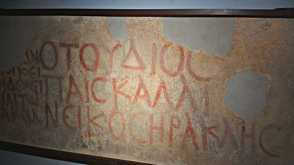 VIII.4.7/VIII.4.6 Pompeii. Red painted graffito from pilaster between doorways.
On display in Naples Archaeological Museum, inv. 4717. Photo courtesy of Giuseppe Ciaramella, June 2017.
Greek text in red letters, according to the Naples Museum information card this translates as:
“Qui abita il figlio di Zeus, Eracle glorioso vincitore; non entri il male” 
“Here dwells the son of Zeus, Heracles the glorious victor; may evil keep out”.      [CIL IV 733]

