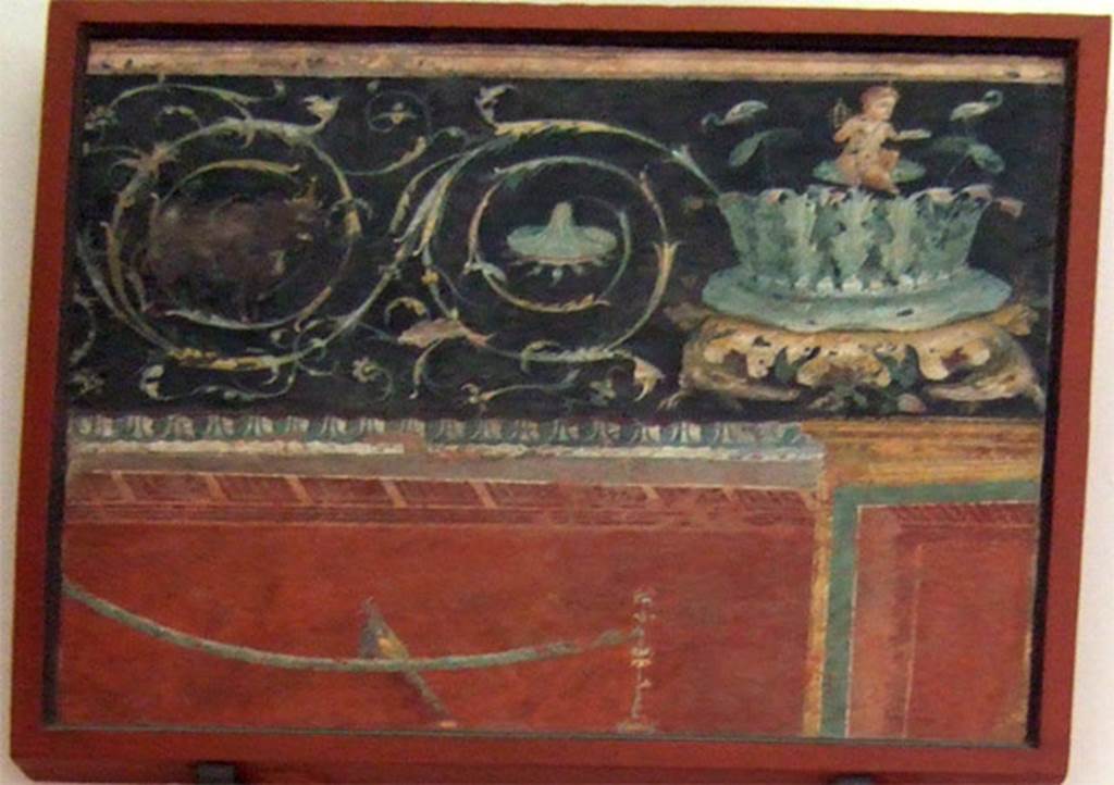 VIII.7.28 Pompeii. Found to the left of the shrine to Harpocrates. Central part of east wall.
Part of an architectural scene with two scrolls with an acanthus bush on the right supported by two crocodiles and on top of it sits a pygmy with a sistrum flanked by two ibis. 
Now in Naples Archaeological Museum. Inventory number 8545.
