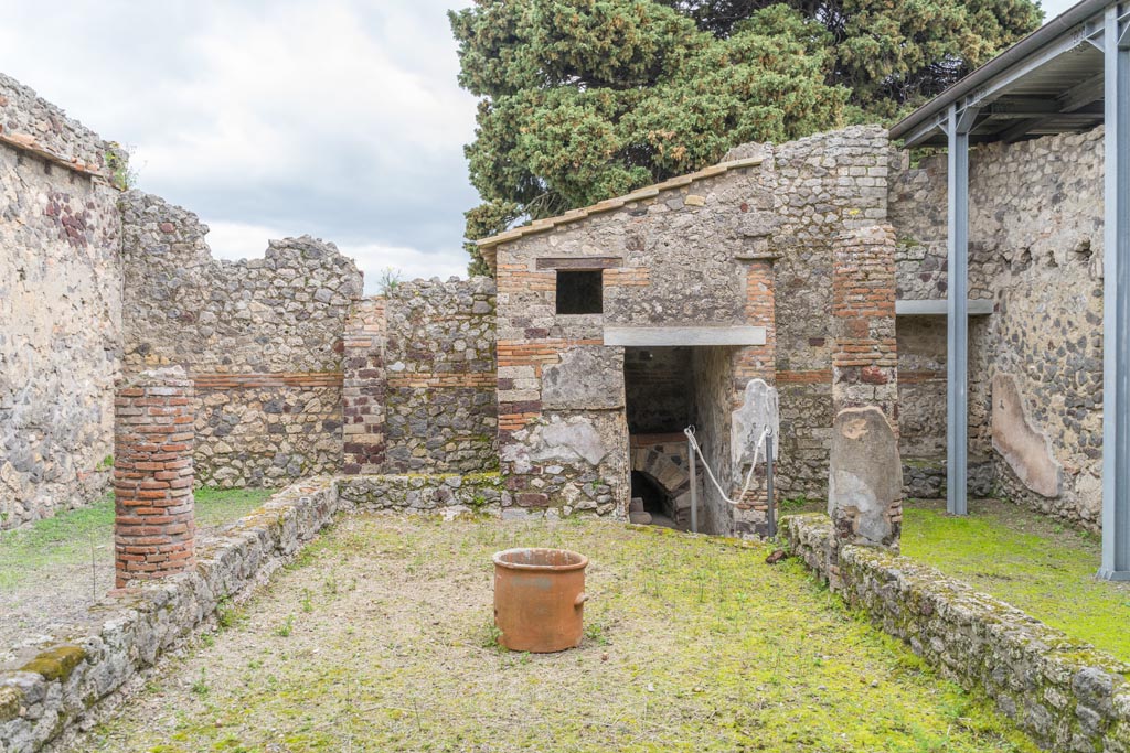 IX.9.c Pompeii. March 2023. Looking east across peristyle garden towards doorway into kitchen. Photo courtesy of Johannes Eber.