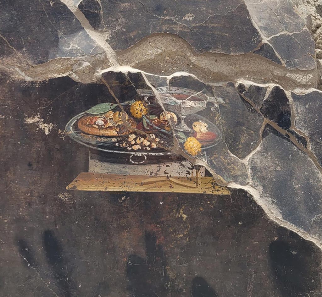 IX.10.1 Pompeii. June 2023. Atrium 2 west wall. Fresco of offering tray.
We have here both the theme of the sacred offering and that of hospitality, albeit indirectly, since eating the frugal meal is a sign of having finally found a hospitable land for the Trojan fugitives.
IX.10.1 Pompeii. Giugno 2023. Atrio 2 parete ovest. Affresco del vassoio delle offerte.
Abbiamo qui sia il tema dell’offerta sacra, sia quello dell’ospitalità, seppure in maniera indiretta, dal momento che il mangiare il pasto frugale è segno di aver finalmente trovato una terra ospitale per i fuggitivi troiani.
Photograph © Parco Archeologico di Pompei.
Vedi/See Una natura morta con xenia dallo scavo della casa IX 10,1 a Pompei. E-journal 3, Scavi di Pompeii, 27.6.2023, p. 6, fig. 2. E-journal on PAP web site 
