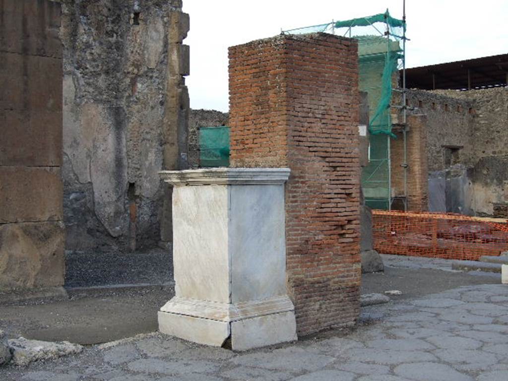 Via dell’Abbondanza, north side, with VII.1.12 in background behind pedestal which was the base of a statue of M. Holconius Rufus.  
December 2006. The statue is now in Naples Archaeological Museum.  
The brick pillar behind it was one of four which supported an arch over Via dell’ Abbondanza.


