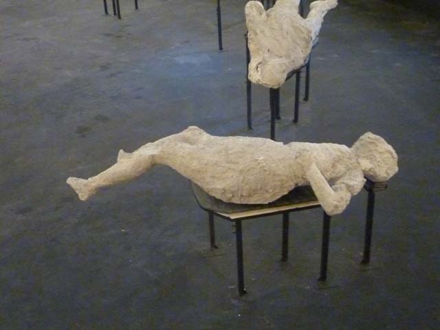 Victim number 4. September 2015. Plaster-cast of victim on display in temporary pyramid in amphitheatre.
According to Dwyer –
The fourth victim was found in the middle of the vicolo, about twenty-five metres from the other three victims.
She was often described as “the pregnant woman”, but her bunched up clothing could have accounted for the impression.
See Dwyer, E., 2010. Pompeii’s Living Statues. Ann Arbor: Univ of Michigan Press, (p.65-69 and fig. 39).
