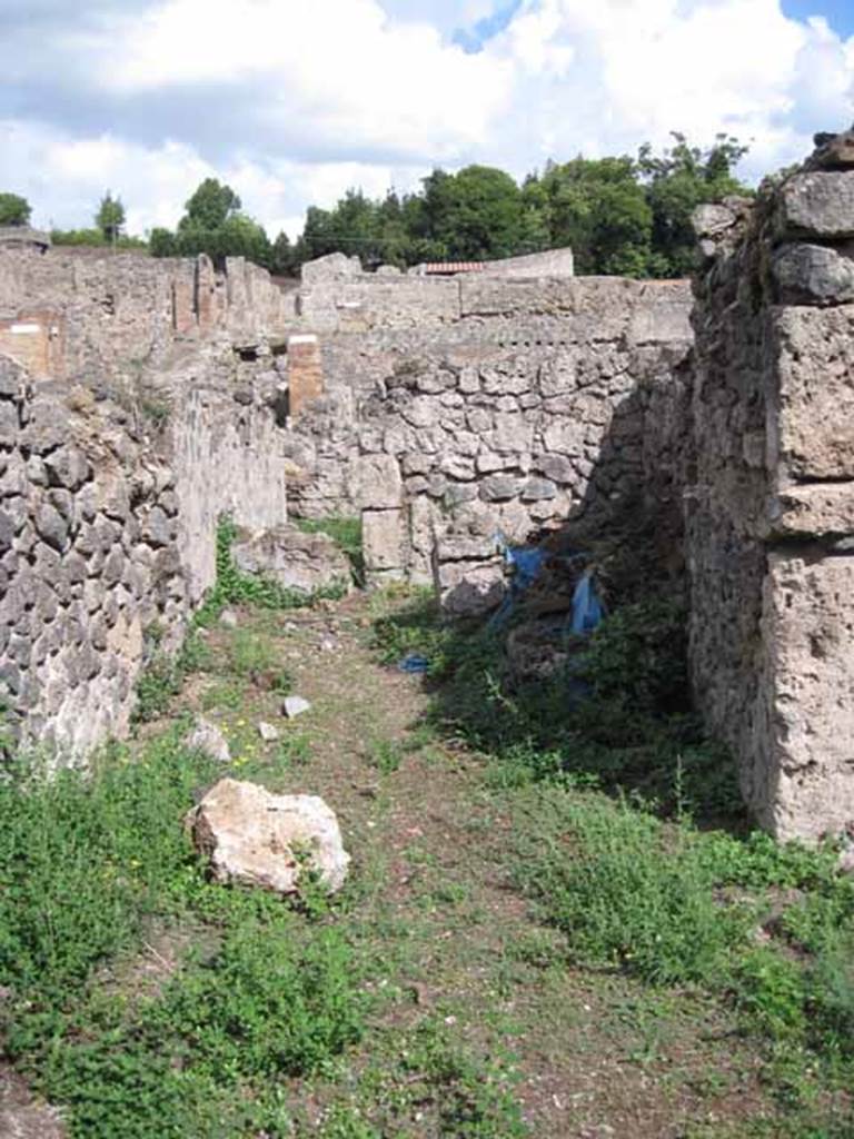 VIII.7.10 Pompeii. September 2010. 
Looking east from garden area towards kitchen, and blocked doorway to corridor leading to entrance on Via Stabiana.
In the south wall (on the right in the shadow) appears to show the remains of a niche, perhaps with a shelf below protruding from the wall.
Photo courtesy of Drew Baker.
According to Boyce (described as VIII.viii.10) –
“In the wall of the kitchen there was a niche and beside it was a lararium painting.
It represented a sacrificial scene with the Genius and the tibicen, one on each side of an altar. On either side of them was a Lar.
In the lower zone was a single serpent beside an altar.
See Boyce G. K., 1937. Corpus of the Lararia of Pompeii. Rome: MAAR 14. (p.78, no.377). 
See Sogliano, A., 1879. Le pitture murali campane scoverte negli anni 1867-79. Napoli: (p.12, no.24, “badly preserved”).
According to Mau  -
“Next to the hearth there was the usual painting of the Lares, and a niche.”
See Mau in BdI, 1875, (p.167) (p.166-169 - La quarta casa). 
