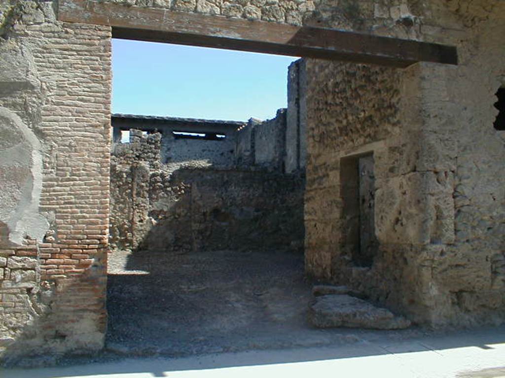 I.7.4 Pompeii. May 2005. Entrance on Via dell’Abbondanza. According to Maiuri, the workshop comprised of a large room on the ground floor, and a smaller room in the north-west corner. This smaller room had a small window in its north wall, onto the roadway, as well as a larger window in its east wall overlooking the vestibule of the workshop. 
Against the west perimeter wall was a masonry kitchen area. Found between the kitchen and the rear wall was the recognisable threshold step and traces in the plaster work of a long and steep wooden stairway that would have led up to the upper floor of the room, and from this led both to the balcony and to the other rooms on the upper floor which covered all the space on the ground floor, where there is no trace of an impluvium or possibility of water drainage. Therefore, the roof would have been totally closed and probably only one layer facing the roadway.  The walls of the ground floor were simply plastered with a clear yellow background with simple red lines forming squares.
See Maiuri, A., 1928. Nuovi Scavi nella Via dell’Abbondanza. Milano: Hoepli. (p.15-16).
