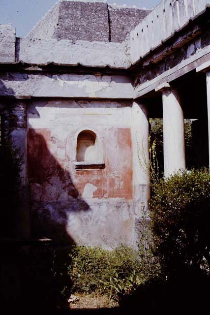 I.7.7 Pompeii. Old undated photograph. Pseudoperistyle, with lararium niche seen in west wall. According to Boyce, the arched niche was adorned with a stucco aedicula façade and a cornice running around the inside walls. The area of the wall immediately around the niche was painted as part of the decoration, into which the niche was set in a panel. There was no lararium painting and no other indication of religious use. It is called an edicoletta larare in the report and probably was a shrine, as there is none elsewhere in the house. Not. Scavi, 1927, 27.
See Boyce G. K., 1937. Corpus of the Lararia of Pompeii. Rome: MAAR 14. (p.25, no.39) 
