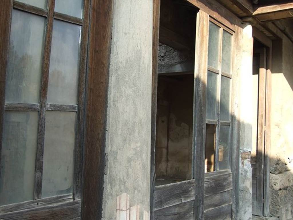 I.7.11 Pompeii. December 2006. South end of house, north wall of north portico with reproduction wooden doors, leading from I.7.12. According to Jashemski, Maiuri said the space between the columns and the west pillar of the portico were closed by glass set in a wooden frame. This would have kept the rain and sun from the triclinium, tablinum and exedra. Maiuri did not mention finding any glass and some scholars think that wooden shutters were used. See Jashemski, W. F., 1993. The Gardens of Pompeii, Volume II: Appendices. New York: Caratzas. (p.38)
From now on, the photos show the northern part of this house, starting from the north wall of the north portico. To see the southern part of the house and garden area, see I.7.12

