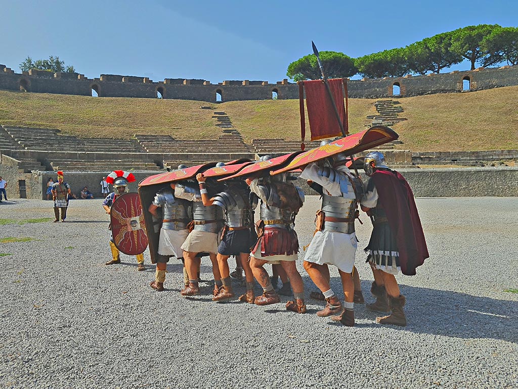 II.6 Pompeii. September 2024. Roman Soldiers – attacking action – testudo/tortoise formation. 
This was slow-moving, but almost impenetrable to enemy fire, and thus very effective during sieges and/or when facing off against enemy archers.
Cohorts approached the city's wall in testudo formation, bringing up battering rams and ladders to breach the gates and scale the walls.
However, the testudo formation did not allow for effective close combat – therefore it was used only when the enemy were far enough away.
Photo courtesy of Giuseppe Ciaramella.

