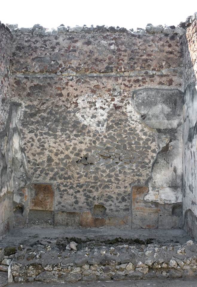 V.1.7 Pompeii. March 2009. Niche on east wall of the peristyle.
According to Boyce the niche was coated with white stucco and in its floor were three holes for statuettes. It used to have several iron nails driven into the wall beside the niche at the level of its floor. Perhaps this was to hold in place an ornamental cornice of wood, as suggested by Mau.
See Boyce G. K., 1937. Corpus of the Lararia of Pompeii. Rome: MAAR 14.  (p.32)

