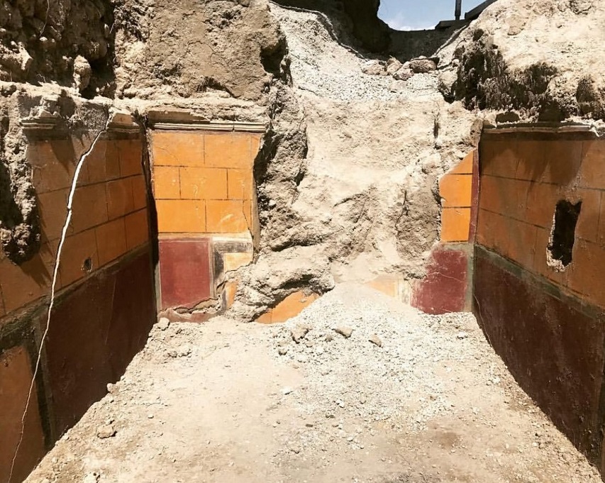 V.2.Pompeii. Casa di Orione. March 2019. 
Room A13, the south ala, on right with white walls showing Orion mosaic floor, the room was open onto the atrium.
Photograph © Parco Archeologico di Pompei.
At the time of the eruption this was a room filled with cupboards, and would have been used like the nearby room, as a storeroom.
The observation of the dynamics of entry of the pumice-stone, together with the finding of glass vases and ceramics buried inside the lapilli, at a height much higher than the floor, allow us to identify the presence of wooden furniture occupying the space (which at the beginning of the eruption had prevented the lapilli from filling the room completely). 
Also on the ground, near the two walls facing east and west there was a rich quantity of pots from table and storeroom, evidently accumulated here, due to the work in progress elsewhere. 
See Osanna M, 2019. Pompei. Il tempo ritrovato. Le Nuove Scoperte. Milano: Rizzoli, (p.101).

