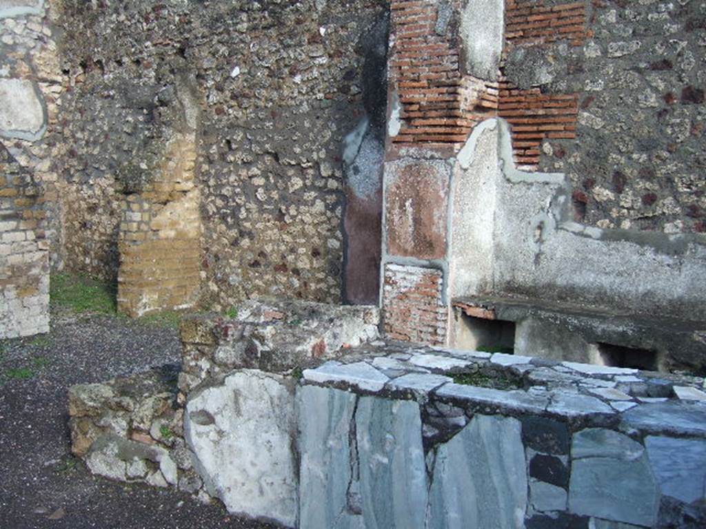 VI.3.20 Pompeii. December 2005. Counter with hearth at end. According to Dyer:
“At the angle of two streets, just behind the fountain, was a small shop, called by some a thermopolium, or shop for the sale of hot drinks. The walls were gaudily painted in blue panels with red borders, and towards the street was a counter cased with marble. The stains left on these counters, apparently by wet drinking-glasses, have led to the identification, or supposed identification, of several such shops.”
See Dyer, T., 1867. The Ruins of Pompeii. London: Bell and Daldy.  (p.49)
According to Breton: This bar of Fortunata had a counter of masonry which held several large terracotta containers, and was covered with a marble tablet, where the footprints of cups/glasses could still be recognised. The liquids contained in them must have contained some acid principle which had attacked the polish of the marble. At the rear was a higher area which held the brazier for heating various beverages.”
See Breton, E; Pompeia, decrite et dessine, 1855, (p.219)
