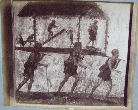 VI.7.9 Pompeii. Wall painting of the Procession of the Carpenters.   
Originally found on pilaster between entrances VI.7.8 and VI.7.9.
Now in Naples Archaeological Museum. Inventory number 8991.
See Helbig, W., 1868. Wandgemälde der vom Vesuv verschütteten Städte Campaniens. Leipzig: Breitkopf und Härtel. (1480).  
According to Leach, figures of Minerva, Mercury and Daedalus painted on its exterior pilasters (6.7.8-12), as well as another painting of a procession advertising the craft of Daedalus under the protection of Minerva and Mercury, were taken by Mau as an indication that this was a Carpenter’s workshop. 
The sign showed 3 carpenters bearing a ferculum that included a figure of Daedalus and some workmen performing carpenters’ tasks.   
A dead figure lies before Daedalus’s feet: this may well be a reference to the nephew Perdix whom the legendary artisan murdered through jealousy for his invention of the rake.   
(PPM 4, p389-91, however, suggested that the sign indicated a perfumer’s shop that dealt in spices requisite to funeral rituals). 
See Leach, E.W: The Social Life of Painting in Ancient Rome and on the Bay of Naples.

