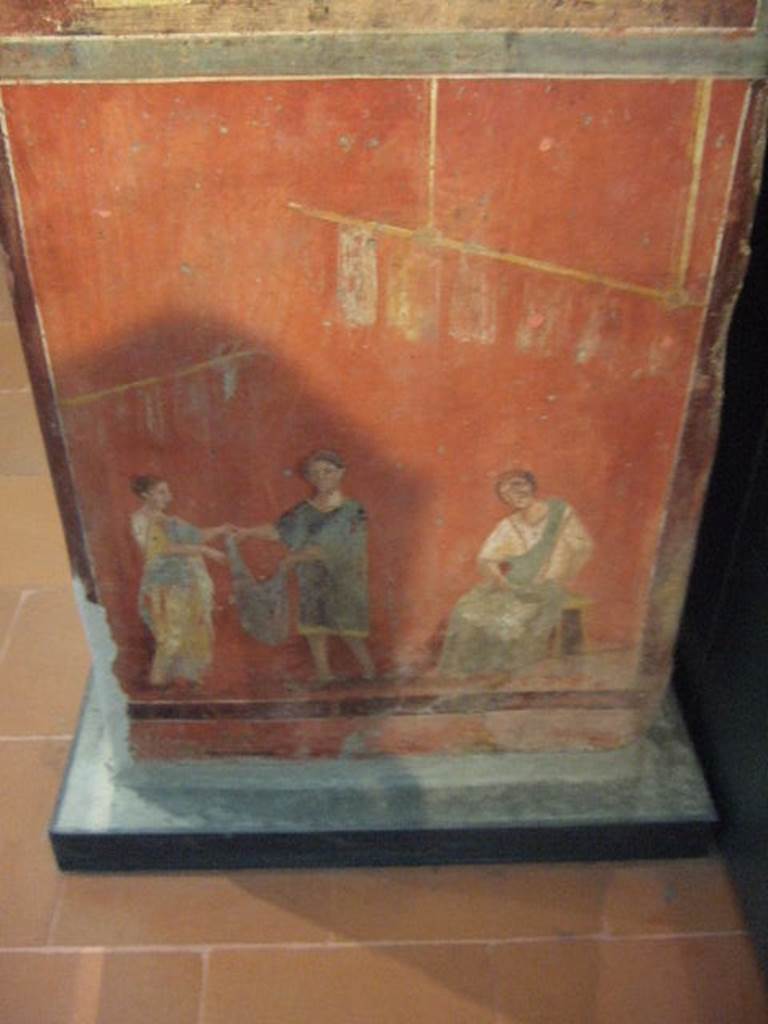Pillar found in the Fullonica at VI.8.20.   Painting of a woman collecting a garment, several of which are seen suspended on high on sticks.  A woman, sitting, is cleaning the instrument for carding. Now in Naples Archaeological Museum.  Inventory number 9974.
