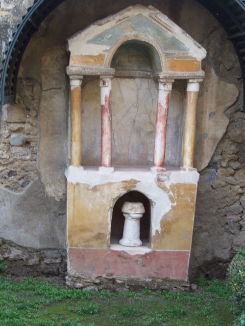 VI.15.8 Pompeii. December 2007. Household shrine in the garden.
According to Boyce, against the west wall of the garden stands an aedicula. It was built upon a high masonry podium coated with yellow stucco. The aedicula is formed by four columns, and two antae applied to the rear wall. These support a roof with pediment. The columns are coated with stucco and painted, the two outer being yellow, the two inner red. The rear wall of the shrine was painted white, as if for a painting but no trace remains. The base is adorned with a red dado and in the centre is cut a large arched recess, painted red within. See Boyce G. K., 1937. Corpus of the Lararia of Pompeii. Rome: MAAR 14. (p.55, np.214, Pl.32,2) 
See Giacobello, F., 2008. Larari Pompeiani: Iconografia e culto dei Lari in ambito domestico.  Milano: LED Edizioni. (p.276)
See Warscher, T., 1925. Pompeji: Ein Führer durch die Ruinen. Berlin und Leipzig: de Gruyter. (p.92)
