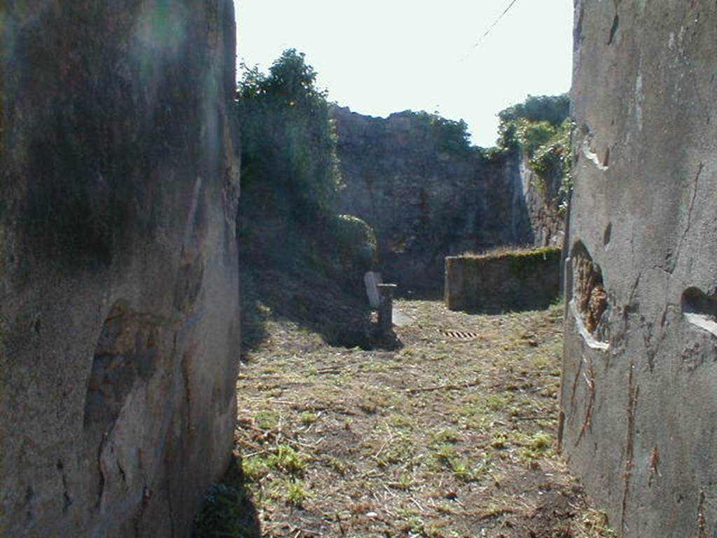 VI.15.12 Pompeii. September 2004. Looking west along entrance corridor across atrium to tablinum/triclinium. According to NdS, the fauces, or entrance corridor, led into the atrium which had an impluvium faced with signinum in its middle. At the head of the impluvium was a travertine monopodium grooved at the front, and on both sides the mouth of a cistern, that to the north-west of the impluvium was covered by a terracotta dolium restored by the ancients, the other in the south-west corner by a low puteal of travertine. Opposite to the entrance was a rather spacious room, probably the triclinium. It had a window overlooking the atrium. See Notizie degli Scavi, June 1897, (p.270)
