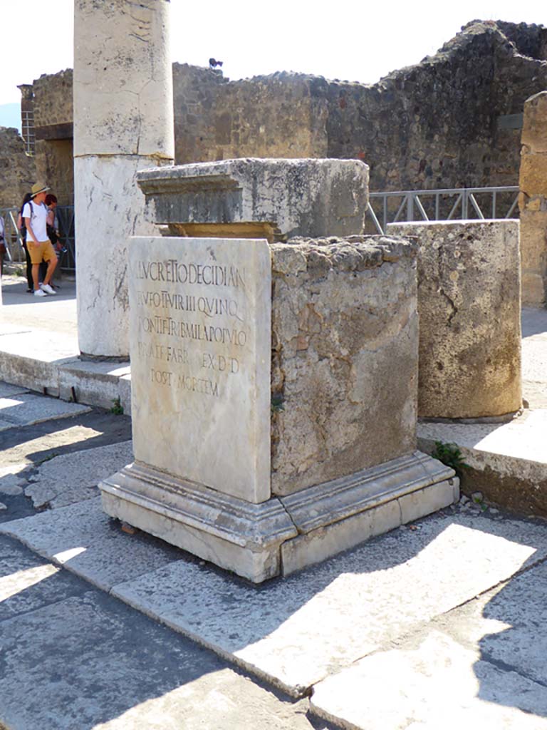 VII.8 Pompeii Forum. June 2019. Pedestal base for statue. Photo courtesy of Buzz Ferebee. This has the Latin inscription –
M . LVCRETIO . DECIDIAN 
RVFO . II . VIR . III . QVINQ
PONTIF . TRIB . MIL .  A POPVLO
PRAEF . FABR . EX . D . D
POST . MORTEM
See Pappalardo, U., 2001. La Descrizione di Pompei per Giuseppe Fiorelli (1875). Napoli: Massa Editore. (p. 101)
According to Pagano and Prisciandaro, this was found in June 1816, it read –
M(arco) Lucretio Decidian(o)
Rufo IIvir(o) III quinq(uennali)
pontif(ici) trib(uno) militum a populo
praef(ecto) fabr(um) ex d(ecreto) d(ecurionum) post mortem       [CIL X 789]
See Pagano, M. and Prisciandaro, R., 2006. Studio sulle provenienze degli oggetti rinvenuti negli scavi borbonici del regno di Napoli. Naples: Nicola Longobardi, (p.114)   PAH III, 7.
According to Berry, Marcus Lucretius Decidianus Rufus had a particularly distinguished career.  The inscription on his statue reads –
To Marcus Lucretius Decidianus Rufus, three times duumvir, (once as) quinquennial duumvir, priest, military tribune by popular decree, military aide-de-camp, in accordance with a decree of the decuriones after his death (CIL X 789)
See Berry, J., 2007. The Complete Pompeii. London: Thames & Hudson. (p.133)

