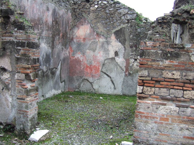 VII.10.5 Pompeii. December 2005. Doorway to room in south-west corner of peristyle, looking towards west wall and south-west corner.  The floor with the diamond design of netting on lavapesto in this room was obliterated by the laying of rough cocciopesto, further indication of the change of use of the entire house gravitating around the peristyle. 
Studi della Soprintendenza archeologica di Pompei, 22: l”Insula VII, 10 di Pompei , by Angelo Amoroso. (p.80)
According to Bragantini et al, red painted plaster could be seen in the middle of the north and east walls. On the south wall, there was a red plinth but the zoccolo was without colour.
In the middle zone was a central aedicula painted with a blue background, the side panels were red. In the upper red zone of the wall, architectural paintings were seen. On the west wall, there was a red plinth and the zoccolo was again colourless, here the central panel was white with red side panels. The upper zone was red.
See Bragantini, de Vos, Badoni, 1986. Pitture e Pavimenti di Pompei, Parte 3. Rome: ICCD. (p.183)
