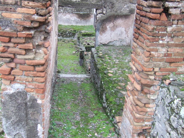 VII.10.5 Pompeii. December 2005. Looking east in rooms leading towards rear entrance doorway at VII.10.13.  According to Amoroso, at the rear of the house, kettles and tubs were installed in a masonry bench. This would seem to indicate that the use of the area was changed perhaps into an “officina lanifricaria”.


