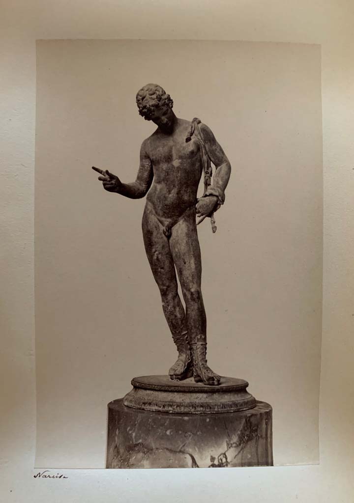 VII.12.17.21 Pompeii. Photograph by M. Amodio, from an album dated April 1878.
Statuette of Narcissus also sometimes described as Dionysus or Pan. Photo courtesy of Rick Bauer.
According to Kuivalainen, this statue (now in Naples Archaeological Museum, inv. no: 5003), had fallen from the upper floor.
“The condition is good, but the original base has been replaced, and the panther is lost.”
He comments – 
“The male’s apparel and the position of the right-hand fingers identifies the bronze as Bacchus dangling a bunch of grapes above a panther.
The iconographic formula is also known from wall paintings in Pompeii.”
See Kuivalainen, I., 2021. The Portrayal of Pompeian Bacchus. Commentationes Humanarum Litterarum 140. Helsinki: Finnish Society of Sciences and Letters, (p.219, H14.)
.
