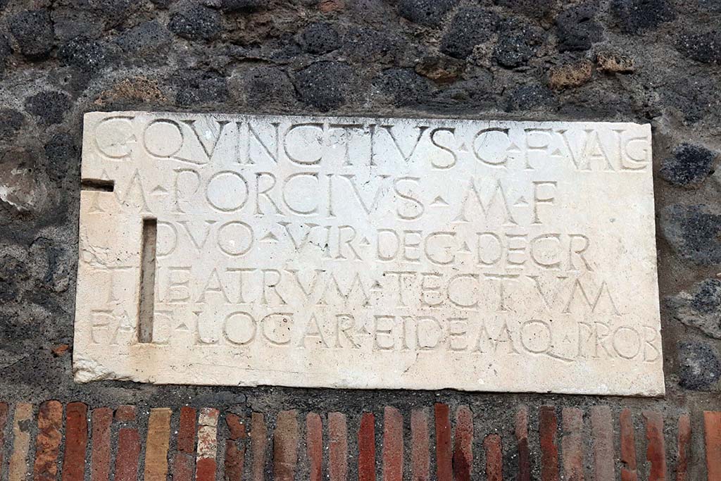 VIII.7.21 Pompeii. September 2017. Dedication plaque above entrance. Photo courtesy of Klaus Heese.
C QVINCTIVS C F VALG
M PORCIVS M F
DVOVIR DEC DECR
THEATRVM TECTVM
FAC LOCA R EIDEMQ PROB      [CIL X 844a]
According to Mau, the names of the builders of the Small Theatre are known from an inscription found in the building.
C. Quinctius C. f. Valg[us], M. Porcius M. f. duovir[i] dec[urionum] decr[eto] theatrum tectum fac[iundum] locar[unt] eidemq[ue] prob[arunt]
“Gaius Quinctius Valgus the son of Gaius, and Marcus Porcius the son of Marcus, duumvirs, in accordance with a decree of the city council let the contract for building the covered theatre and approved the work”.
See Mau, A., 1907, translated by Kelsey F. W. Pompeii: Its Life and Art. New York: Macmillan, (p.153).
According to Cooley, two copies of this inscription were set up near the main entrances to the Covered Theatre. 
See Cooley, A. and M.G.L., 2014. Pompeii and Herculaneum: A Sourcebook. London: Routledge, B11, p. 29-30.
This one is from the entrance on Via Stabiana and a second was from the entrance from the Large Theatre to the Small Theatre.
