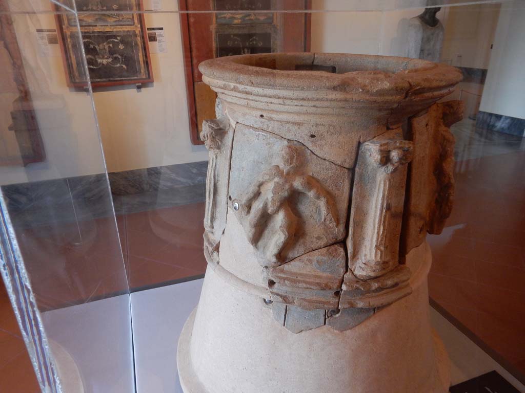 VIII.7.28 Pompeii. June 2019. Terracotta decorated puteal with Hercules in scenes of the rituals of Bacchus.
The upper part has four ionic columns with figured capitals. Between are four figures in relief.
One figure shows Hercules brandishing a club in his right hand while holding a crown in his left.
A youth holds a vase on his left shoulder and looks right towards the third figure.
The third person advances uncertainly, manifested by the enlarged position of legs and arms.
The last figure has the pose of the Hercules urinating, but wears Dionysus's tall boots and holds a tympanum in the left.
It seems to be a Dionysian procession in which the hero participates.
The lower part is decorated with incisions imitating isodomic masonry (blocks with staggered joints).
Found in the area of the pastophorium (priest’s accommodation). Photo courtesy of Buzz Ferebee.
See De Caro S., 2006. Egittomania: Iside e il Mistero. Milano: Electa, p. 117.
