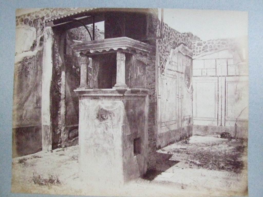 IX.2.26 Pompeii. Lararium situated at south end of east wall of corridor leading to atrium.  
Old undated photograph from Fox collection. Courtesy of Society of Antiquaries. According to Bragantini, the triclinium on the east side of the lararium had a floor of cocciopesto, ornamented with a design in white tesserae. It had a border and in the centre had a circle of white tesserae that was the site of the table.  The north wall had a small window. The walls were painted with a black dado decorated with painted plants. The middle zone of the walls was white, with panels edged with a border separated by narrow compartments with candelabra. The upper zone was probably white, with architectural paintings.
See Bragantini, de Vos, Badoni, 1986. Pitture e Pavimenti di Pompei, Parte 3. Rome: ICCD. (p.425, triclinio ‘c’).
