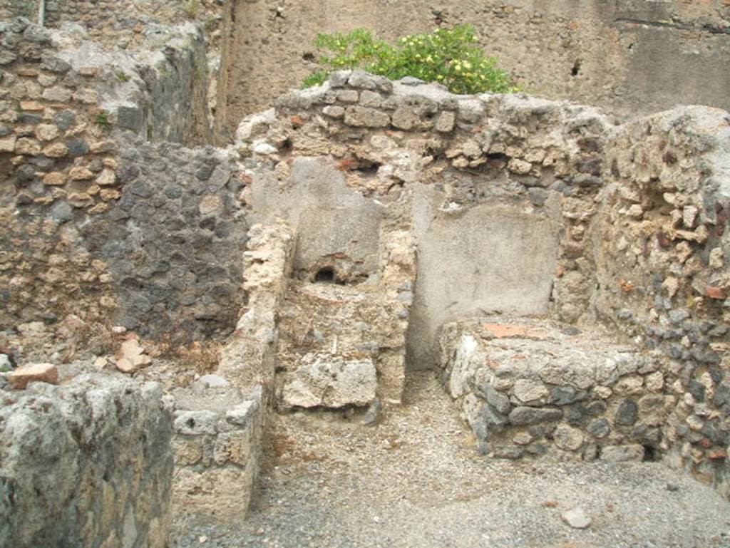 IX.3.12 Pompeii. May 2005. Looking north towards the kitchen and latrine. There were three masonry steps leading up to the latrine, on the left. Nearby, on the right, was the small kitchen area with the remains of the bench for the hearth. At the rear of both areas, the walls were painted with white plaster.
