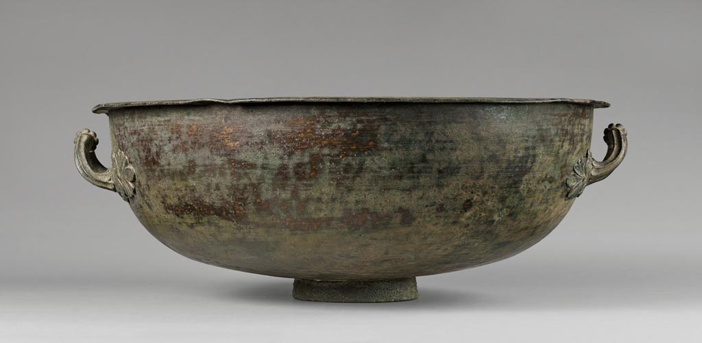 Discovered in a villa in Boscoreale. Bronze basin with palmette handles.
Digital image courtesy of the Getty's Open Content Program. Now in the Getty Museum, inventory number 72.AC.142.
This large basin, which sits on a small, straight-sided foot, is undecorated except for two fluted handles, each encircled at its mid-point with a beaded band. Both handles are attached to the basin with appliques fashioned in the shape of palmettes. This vessel was discovered in a villa at Boscoreale or in the vicinity, although the exact findspot is unknown. 
